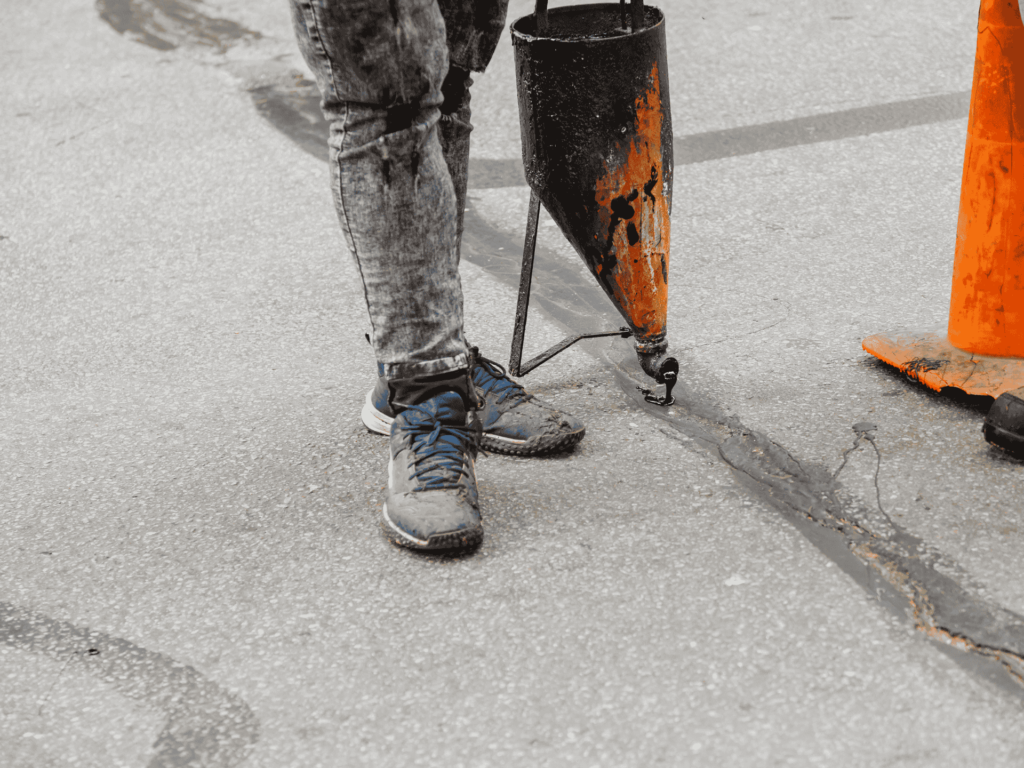 Worker using a crack filler applicator tExperienced paving contractor working on a driveway in Tyler, TXo seal asphalt cracks and prevent further pavement deterioration in Jacksonville, TX.