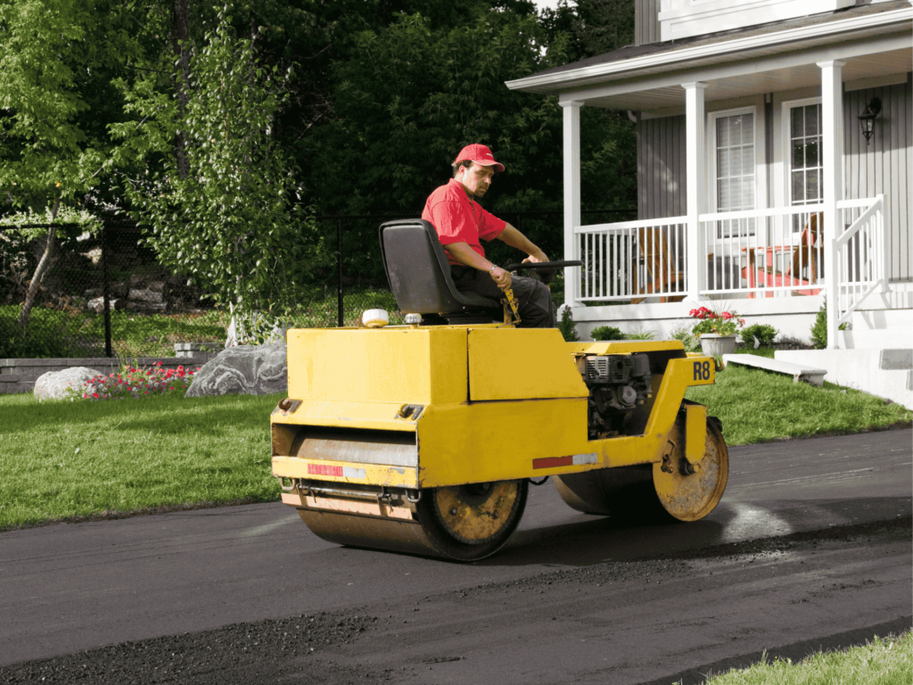 Worker operating a road roller to compact and smooth freshly paved asphalt driveway for a residential home in Jacksonville, TX.