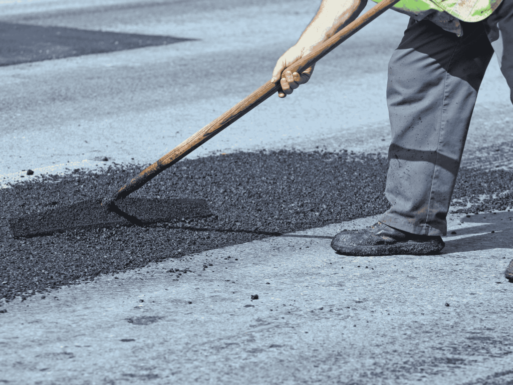 Worker spreading fresh asphalt to fill and repair potholes, ensuring a smooth and safe road surface in Jacksonville, TX.